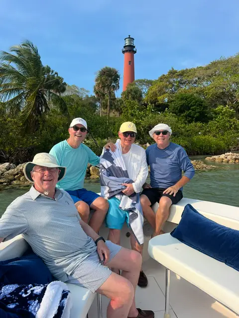 Four friends relaxing on Tom Cat's cushioned bow seating with the red Jupiter Lighthouse behind them